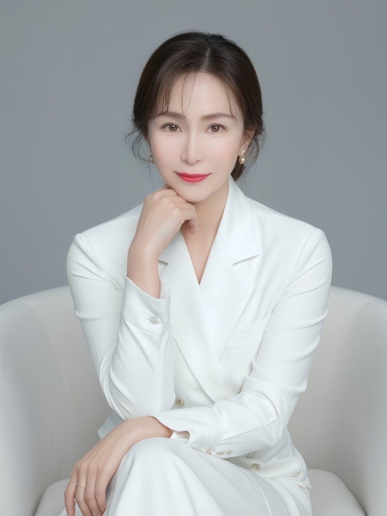 Jingxin Lee, seated in a white suit, one hand resting under her chin.